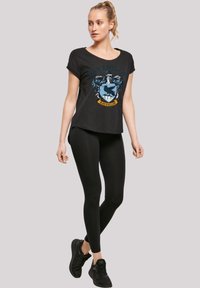 Svart t-skjorte med Ravenclaw-crestdesign, rund hals, korte ermer; kombinert med svarte leggings og svarte joggesko.