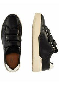 Black leather sneakers feature double Velcro straps, white rubber soles, and a contrasting white toe cap. The design includes minimal detailing.