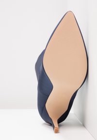 Navyblå spetsig klackskor med satinyta och en slät tan sula med subtila ränder. Slank stilettklackdesign.