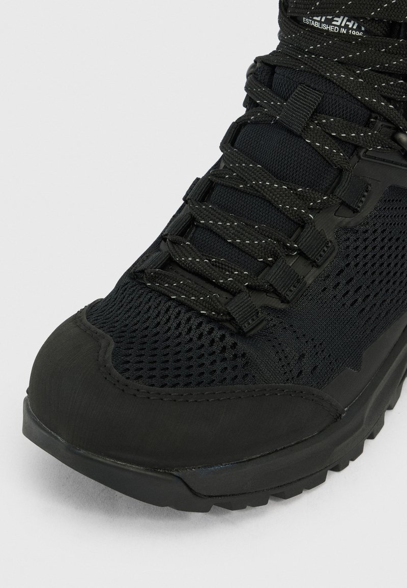 Czarne siateczkowo-rubberowe buty trekkingowe z wzmocnionym czubkiem, grubą podeszwą z bieżnikiem oraz czarnymi sznurowadłami z odblaskowymi włóknami.