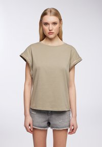 T-shirt corto in khaki, realizzato in un tessuto morbido, con maniche arrotolate e dettagli metallici, abbinato a pantaloni corti grigi usurati.