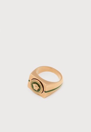 Gouden vierkante ring met een groene inzet, met een leeuw-embleem in het midden en een decoratief Grieks sleutelpatroon eromheen.