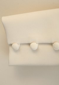 Biały materiałowy worek z trzema zaokrąglonymi guzikami, charakteryzujący się gładką, miękką teksturą i kanciastym designem klapki.