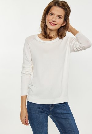White sweater with long sleeves and a wide neckline, made from a soft, lightweight fabric, paired with blue denim jeans.