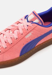 Rózsaszín velúr sneakers lila részletekkel, texturált anyagból, szőtt fűzőkkel és gumitalppal. A logó jól láthatóan van elhelyezve.