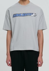 Szara bawełniana koszulka z krótkim rękawem. Z przodu znajduje się niebieska grafika "LOWLIGHTS". Prosty, luźny krój.