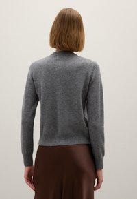 Maglione di lana grigio con maniche lunghe, scollatura rotonda e orlo a costine. Indossato su una gonna di raso marrone. Texture liscia, design aderente.