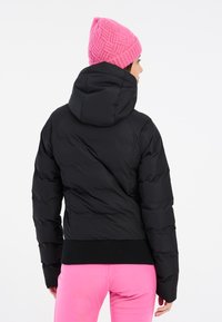 Schwarze Pufferjacke mit Kapuze, die ein gestepptes Design und gerippte Bündchen aufweist, getragen mit einer rosa gestrickten Mütze. Die Rückansicht zeigt die Kontur und Passform.