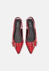 Červené vegan kožené slingback topánky s špicatými špičkami, lesklým povrchom a prackou so kovovými okami. Čierne vložky sú viditeľné.