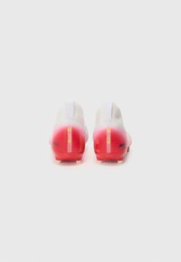 Bottes de football en dégradé blanc et rouge, avec un design épuré, une texture lisse, un talon renforcé et un branding distinct sur le côté.