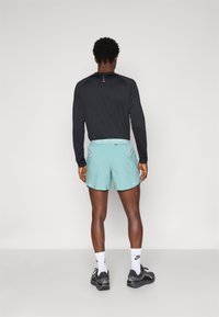 Heren sportkleding bestaande uit een zwart langemouwen top en mintgroene shorts, gemaakt van zacht, lichtgewicht materiaal. De shorts hebben een verstelbare taille met een trekkoord.
