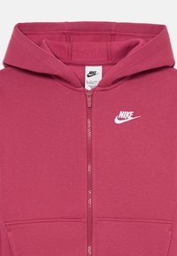 Fleece marrom com fecho, feito de tecido macio, com um bolso canguru e o logótipo branco da Nike bordado no lado esquerdo do peito.