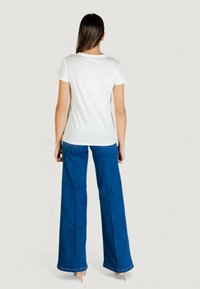 Biała koszulka z krótkim rękawem zestawiona z wysokim stanem i szerokimi nogawkami niebieskich dżinsów. Strój cechuje się prostym designem i luźnym krojem.