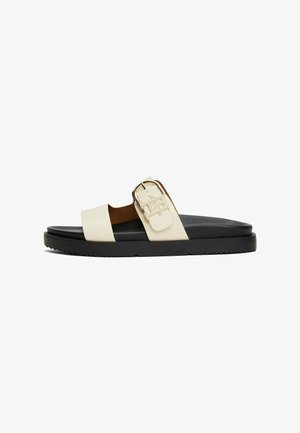Slide sandal i creme og sort. Har en bred rem med en guldfarvet spænde og tekstureret sål for godt greb. Materialet er glat.
