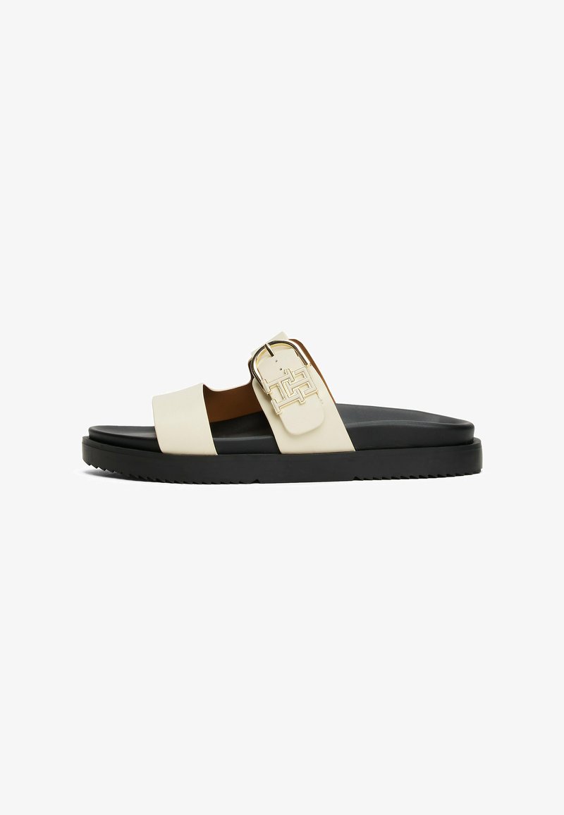 Sandalia deslizante en crema y negro. Presenta una correa ancha con un hebilla en tono dorado y una suela texturizada para mayor agarre. El material es suave.