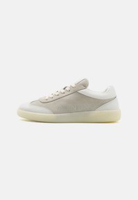 Lærsneakers i off-white og lys beige, med en suede panel, snøring og preget logo på siden. Flat gummisåle.