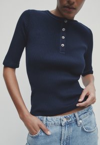 Marineblå ribbet t-shirt med kort ærme og rund halsudskæring samt fem-knaps lukning, sammen med højtaljede lyseblå denim shorts.