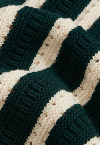 Couverture en tricot avec des rayures alternées vert foncé et crème. Un motif texturé avec des zones en relief et des sections lisses crée de la profondeur.