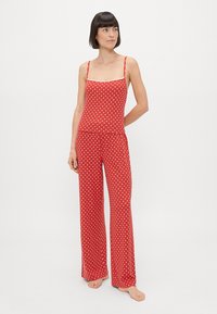 Red polka dot pajama set featuring a sleeveless top with thin straps and wide-leg pants. Fabric appears soft with a smooth texture.