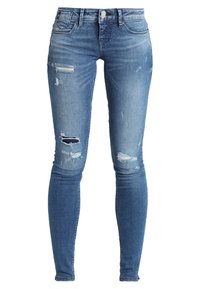 Jeans ajustados en denim azul medio con zonas desgastadas, roturas en las rodillas, cinco bolsillos y un cierre clásico de botón y cremallera.