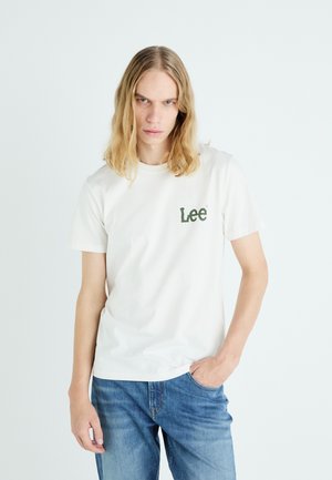 Fehér pamut póló, amelyen egy zöld "Lee" logó található a bal mellen, kék farmernadrággal párosítva. Egyszerű, kerek nyakú dizájn.
