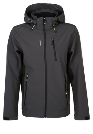 Hombre vestido con chaqueta con capucha gris oscuro y pantalones de exterior de color naranja brillante y negro con zapatos de senderismo negros, de pie frente a un fondo liso.