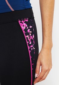 Leggings de sport noirs avec un motif géométrique rose sur le côté, mettant en valeur une texture lisse et un design ajusté.