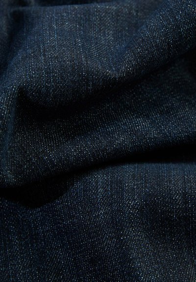 Tela de mezclilla azul oscuro con un tejido fino y texturizado; presenta sutiles destellos claros que crean profundidad visual. Material suave y flexible.
