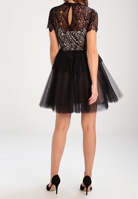 Svart cocktailklänning med spetsöverdel och korta ärmar samt en nyckelhålsdetalj i ryggen, i kombination med en lager-på-lager tyllkjol.