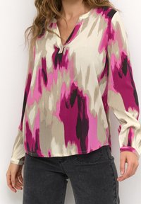 Blouse à manches longues en tissu léger à motifs avec des nuances de rose, crème et noir, présentant une texture et un col en V.