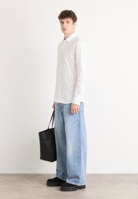 Camisa blanca de botones, pantalones vaqueros de pierna ancha de denim azul claro y relajado, bolso tote negro y zapatos negros gruesos. Diseño simple y limpio con colores neutros.
