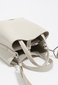 Bolso de mano de cuero beige con dos asas, bolsillo interior con cremallera y cierre a presión. Textura suave, diseño minimalista y detalles en metal plateado.