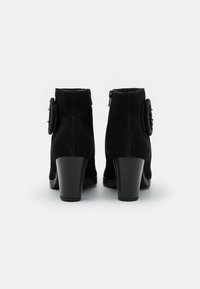 Botines de ante negro con un alto tacón cuadrado, cierre de cremallera y detalle decorativo de tela en forma de flor en el lado.