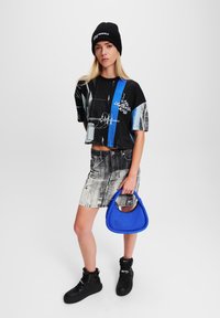 Fekete és kék crop top, megkoptatott farmer szoknya, kék táska, fekete magas szárú sportcipők, fekete kötött sapka, modell álló helyzetben.