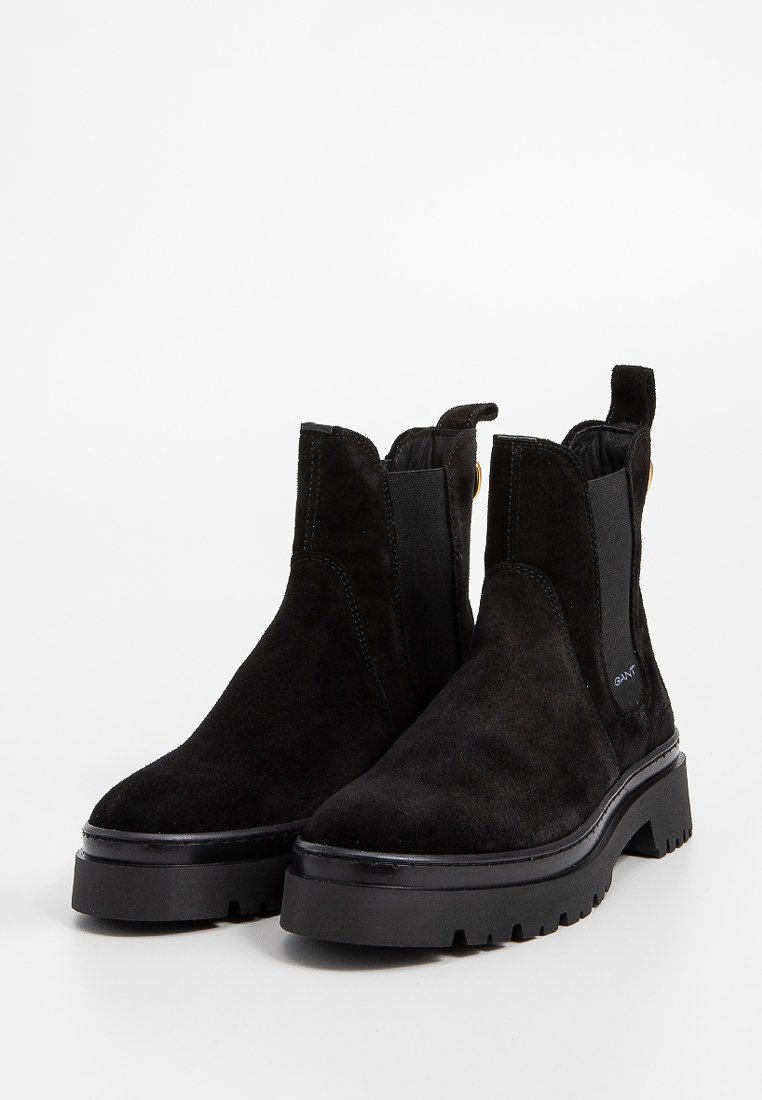 Schwarze Wildleder-Ankle-Boots mit elastischen Seitenpanels, chunky schwarzer Sohle und minimaler Markenkennzeichnung. Sie haben eine glatte Textur und eine abgerundete Zehenpartie.