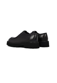 Zapatos de cuero negros con un acabado suave, puntera redondeada y suelas gruesas y texturizadas. Diseño minimalista sin hardware visible.