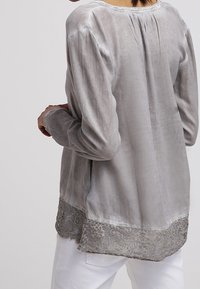 Blouse grise à manches longues en tissu doux, dotée d'une délicate bordure en dentelle au bas et d'une coupe légèrement ample.