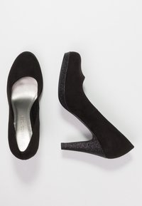 Des chaussures à talons hauts en daim noir avec un bout arrondi et un talon en paillettes noires texturé. L'intérieur est doublé d'un argent métallique.
