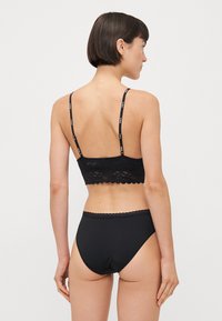 Black lingerie set featuring a lace bralette with scalloped edges and adjustable straps, paired with high-waisted, seamless black briefs.