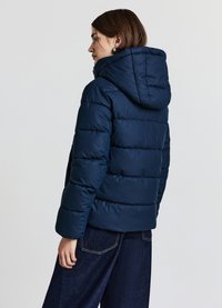 Giacca imbottita blu navy con cappuccio, caratterizzata da un design trapuntato e polsini elasticizzati. Il tessuto appare liscio e idrorepellente.