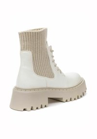 White ankle boots with a ribbed beige knit collar, round toe, and chunky textured sole. Lace-up design with a smooth leather finish.