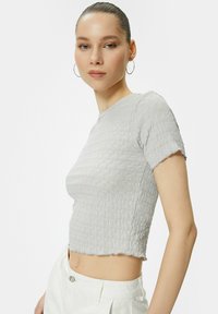 Grå cropped T-shirt med et struktureret, bølget mønster, korte ærmer og rå kant. Stoffet har et let strækbart udseende.
