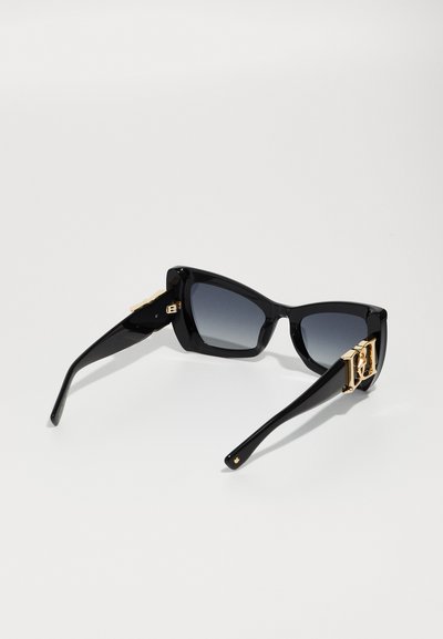 Lunettes de soleil noires en forme de œil de chat avec des verres dégradés et des accents en doré sur les branches. Fini brillant avec des bords lisses.