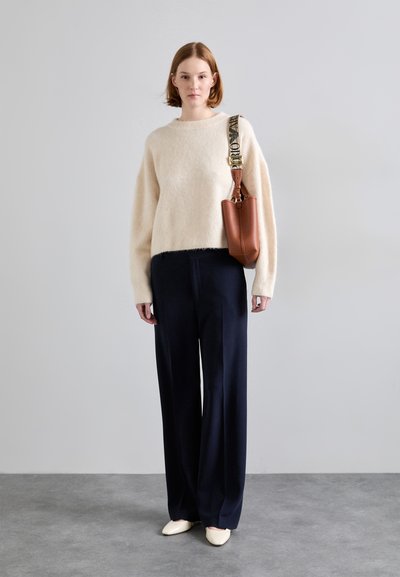 Pull crémeux et duveteux avec un col rond ; pantalon large bleu marine ; sac marron avec une bandoulière à motif ; chaussures pointues pâles.