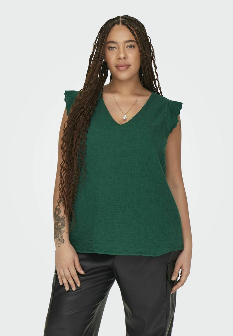 Top verde sin mangas con escote en V, que presenta detalles de hombros con volantes y una tela texturizada. Combinado con pantalones de cuero negros.