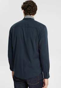 Marineblauwe shirt met lange mouwen, contrasterende grijze kraag, met knoopsluitingen aan de manchetten en een afgeronde zoom, gemaakt van zachte stof met een gladde textuur.