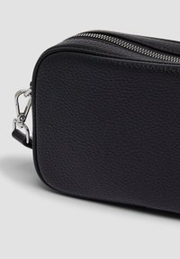Borsa nera in pelle con superficie testurizzata, forma rettangolare, cerniera argentata e attacco per tracolla removibile. Gli accessori includono una clip metallica.