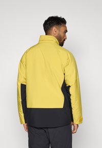 Vandeniui atsparus džemperis ryškiai geltonos ir juodos spalvos. Pasižymi aukštu apykaklė, kontrastingomis šoninėmis juostomis ir tekstūruotu akcentu ant rankogalių.