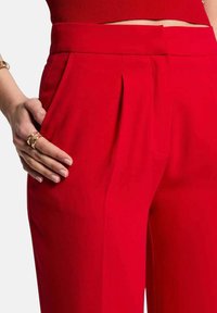 Los pantalones ajustados rojos cuentan con una cintura alta, pliegues en la parte delantera, bolsillos laterales y una textura de tela suave.