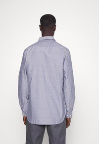 Vaaleansininen napillinen paita, jossa on kaulus, pitkät hihat ja kaareva helma. Sisältää teksturoitua kangasta ja nappikoristeet hihansuissa.